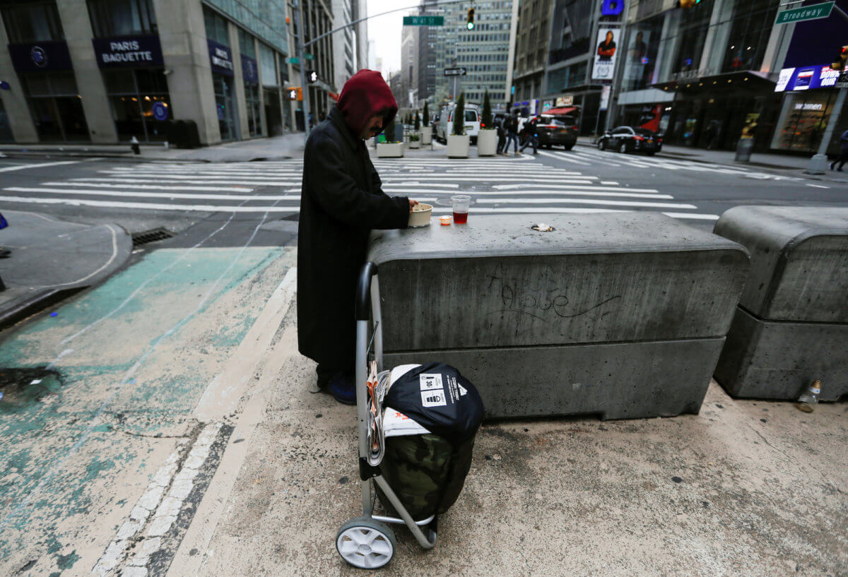 A homeless man eats while standing on a corner along a nearly empty Broadway in midtown Manhattan during the coronavirus outbreak in New York