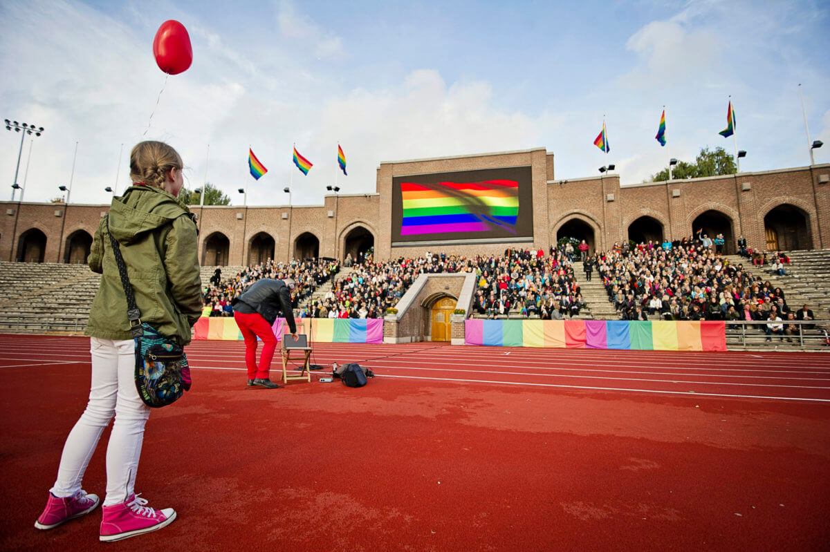 People sing the Russian national anthem while raising rainbow flags at the Stockholm Olympic Stadium