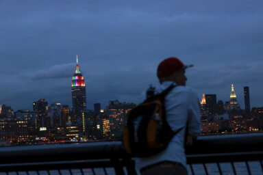A man watches the skyline of Manhattan as the Empire State Building is lit in rainbow colors during the celebration of the annual Gay Pride Parade in New York