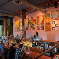 Patrons discuss Craig Anthony Miller’s (aka CAM) artwork on the wall from their bar stool at Superfine’s sunken bar in September 2022.