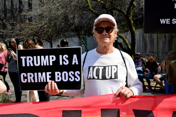 Robert Croonquist, donning an ACT UP shirt, holds the banner and a sign.