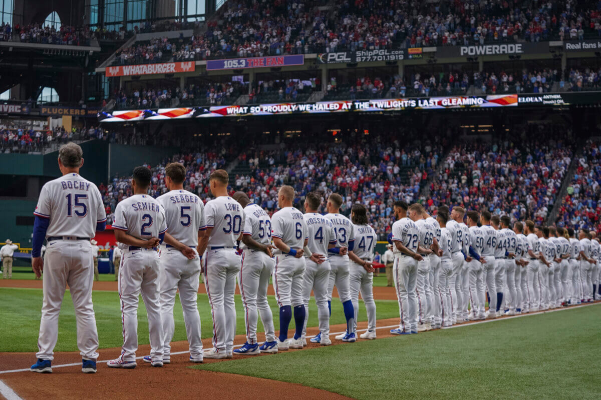 The Texas Rangers stand for the national anthem before an opening day baseball game against the Philadelphia Phillies, March 30, 2023, in Arlington, Texas.