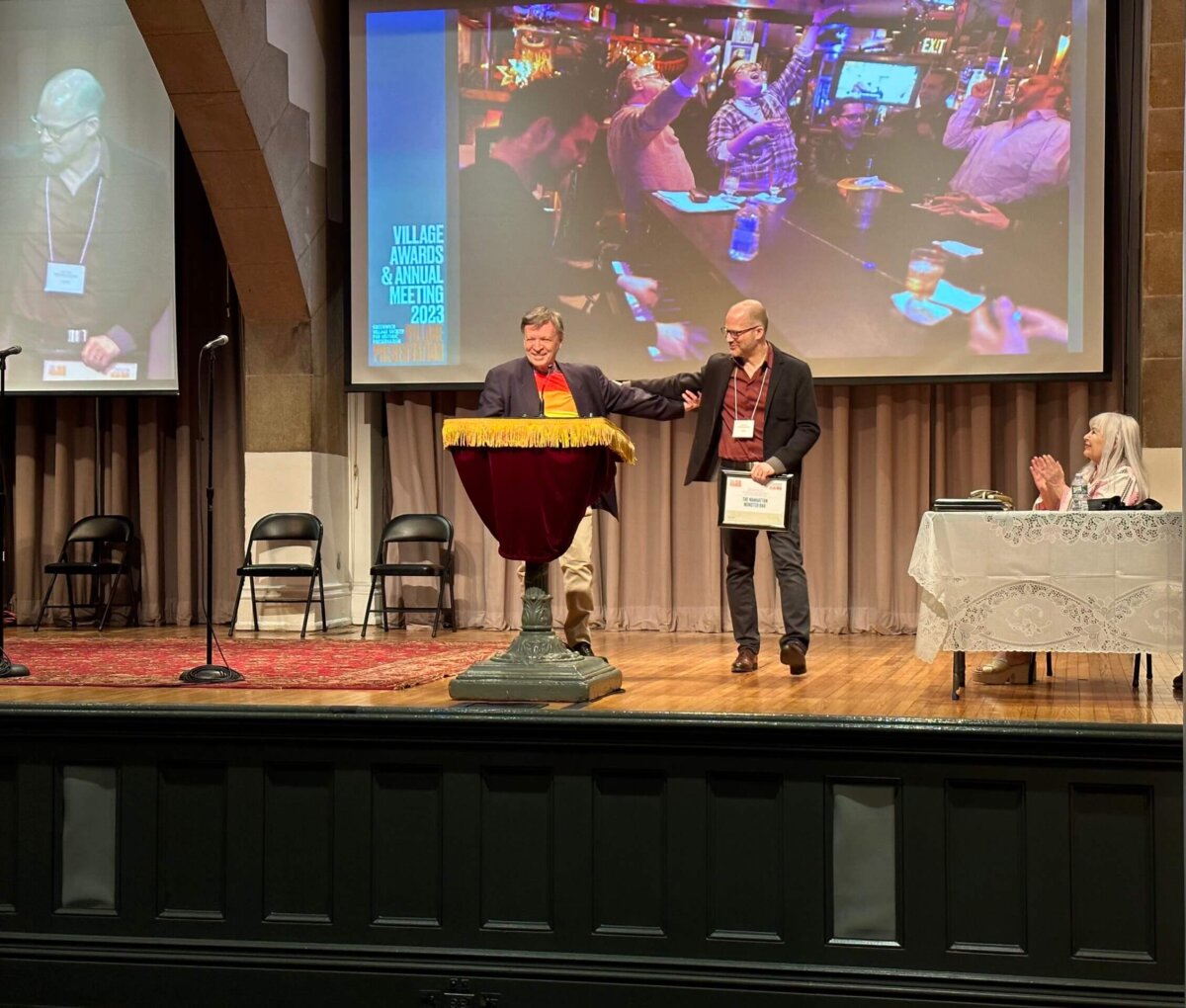 Musician Martin St. Lawrence (left) and general manager Daniel Tobey (right) accept the 2023 Village Award for The Monster Bar from Village Preservation at Cooper Union’s Great Hall on June 13. Penny Arcade (seated, far right) emceed the event.