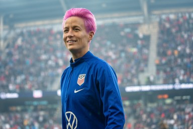 Former soccer star Megan Rapinoe smiles while standing on a field.