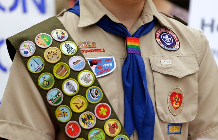 Merit badges and a rainbow-colored neckerchief slider are affixed on a Boy Scout uniform outside the headquarters of Amazon in Seattle. The U.S. organization, which now welcomes girls into the program and allows them to work toward the coveted Eagle Scout rank, announced Tuesday, May 7, 2024, that it will change its name to Scouting America as it focuses on inclusion.