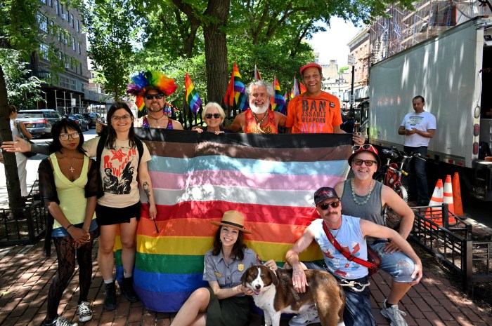 Participants of the flag-raising ceremony — including a dog — surround the large Rainbow Flag before raising it up.