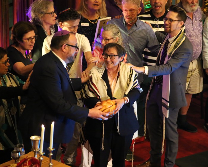 The new Rabbi Jason Klein and retiring Rabbi Sharon Kleinbaum hold the challah bread together on stage at the Congregation Beit Simchat Torah Pride Shabbat on June 28.