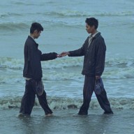 Two men greet each other in a scene in "Viet and Nam" near the ocean.