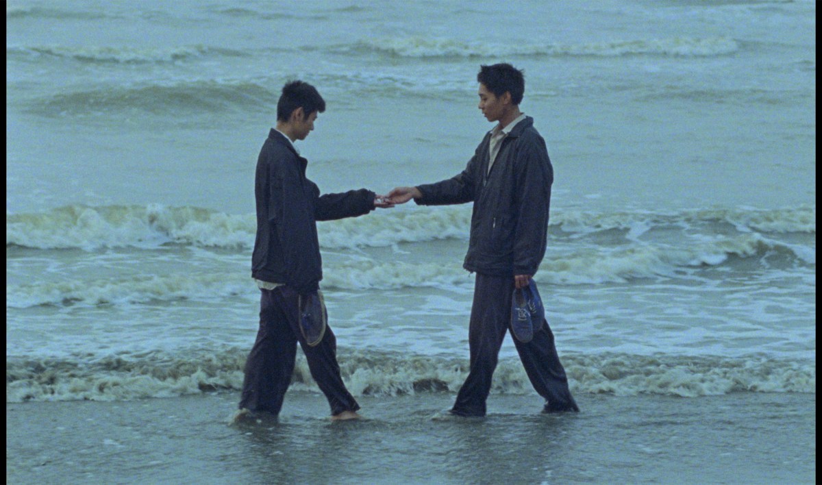 Two men greet each other in a scene in "Viet and Nam" near the ocean.