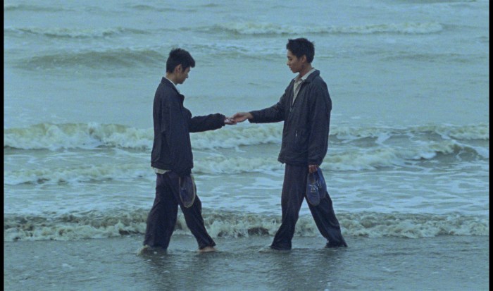 Two men greet each other in a scene in "Viet and Nam" near the ocean.