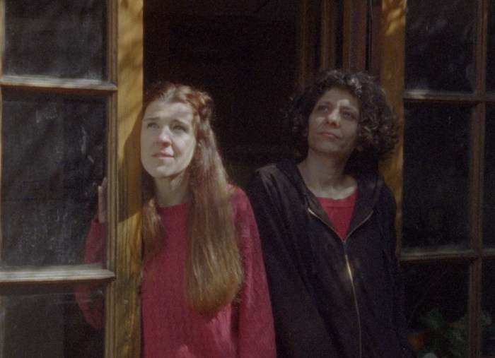 Two women stand outside while staring upward.