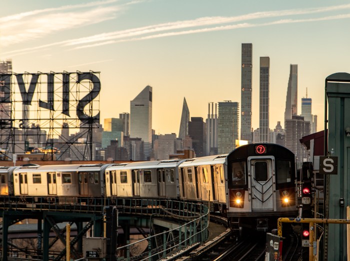 The New York City skyline is visible at sunset as the 7 subway train approaches.