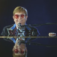 Elton John smiles while sitting at a piano.
