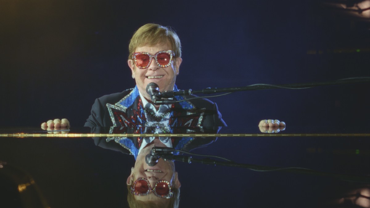 Elton John smiles while sitting at a piano.