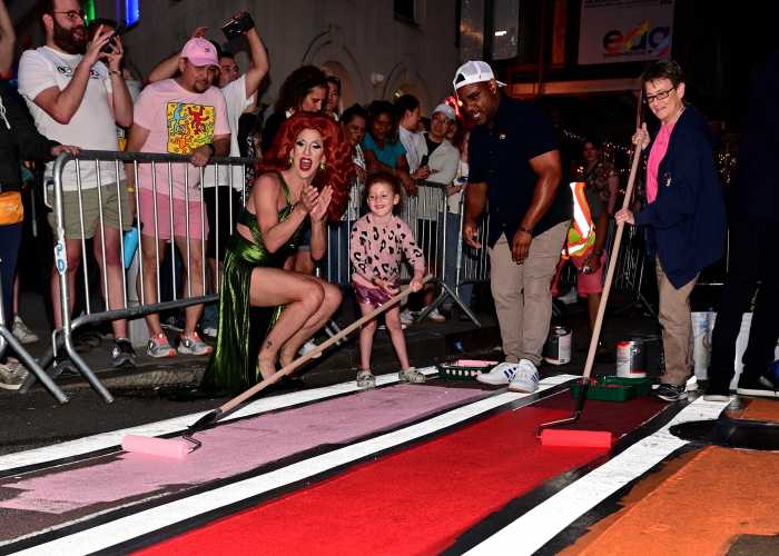 Drag artist Marti Gould Cummings cheers on while a young helper paints the crosswalk.