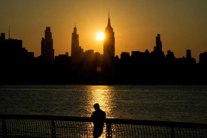 The sun rises behind the Empire State Building and the New York City skyline as a person stands along the riverfront in Hoboken, New Jersey, U.S., July 25, 2025.