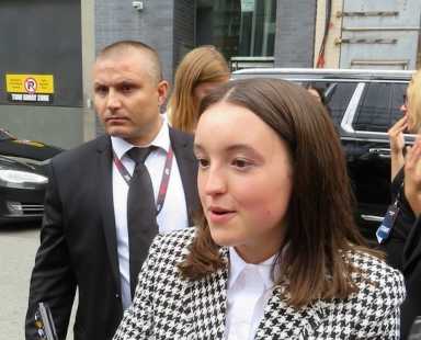 Bella Ramsey speaks to reporters. A person in a suit is standing in the background.