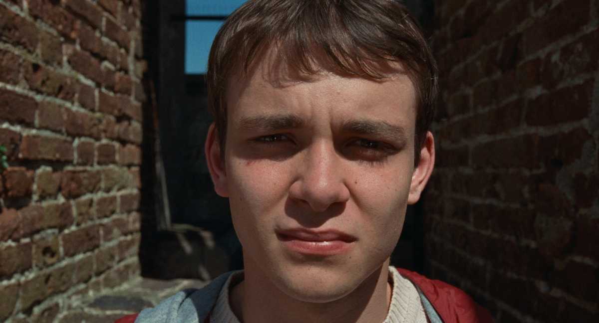 A teenager looks into the camera while facing the sun in a close-up view.