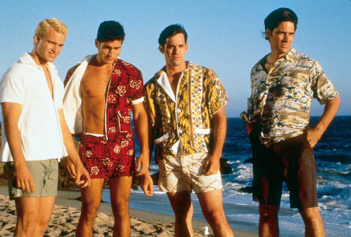 Four men stand together on a beach while facing the sun.