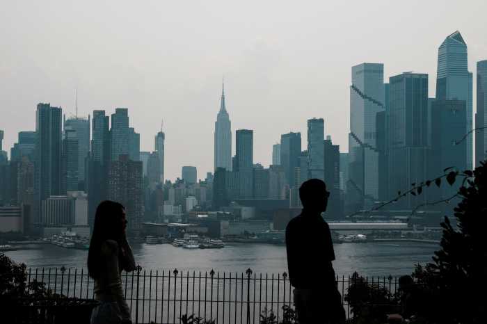 People walk at a local park while haze and smoke caused by wildfires in Canada linger over the skyline of midtown Manhattan in New York City, as seen from Weehawken, New Jersey, U.S., August 5, 2025. REUTERS/Eduardo Munoz