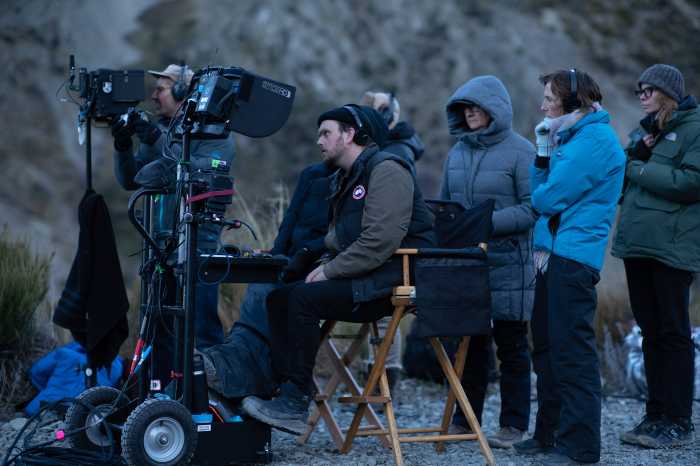 Samuel Van Grinsven sits down among several other people who are all wearing jackets during a behind-the-scenes filming of "Went Up The Hill."