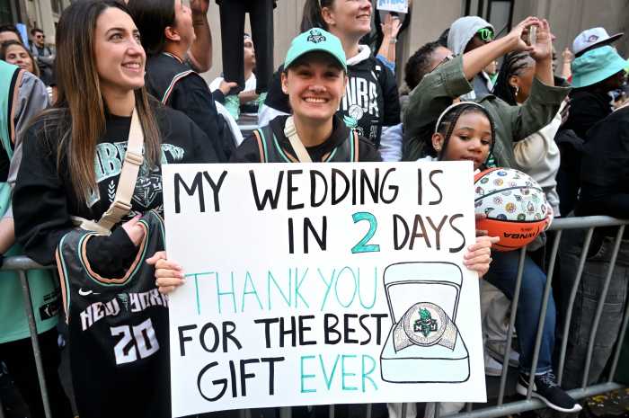 An individual holds a sign that reads: "My wedding is in 2 days. Thank you for the best gift ever." The sign features a New York Liberty championship ring. The subject is smiling while surrounded by the crowd.