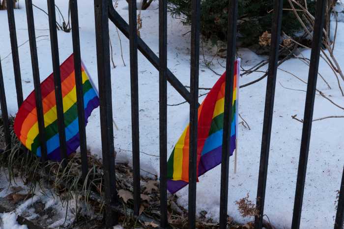 Rainbow Flags in the snow along the fence at the park.