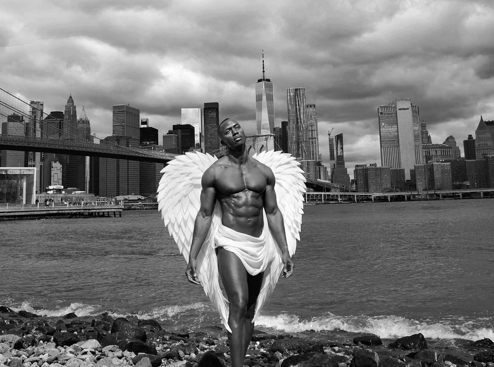 An angel stands at the edge of the East River against the backdrop of the Manhattan skyline.