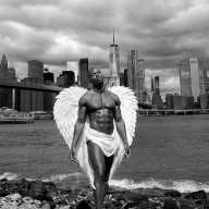 An angel stands at the edge of the East River against the backdrop of the Manhattan skyline.