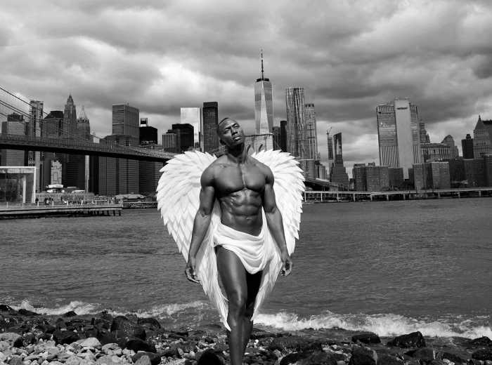 An angel stands at the edge of the East River against the backdrop of the Manhattan skyline.