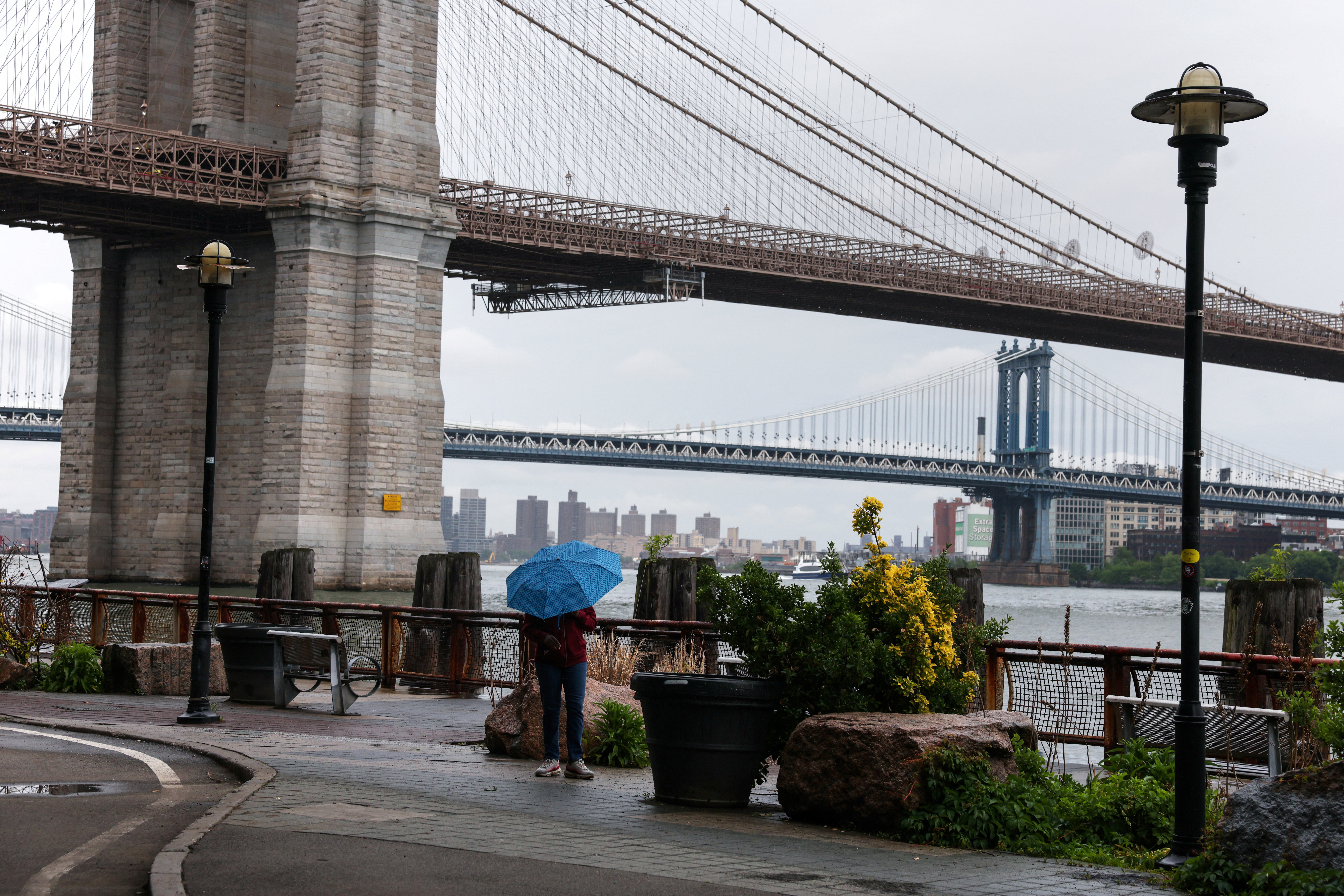A woman stands with an umbrella near the Brooklyn Bridge during rainy weather in New York City, U.S., May 21, 2026.