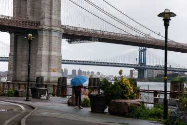A woman stands with an umbrella near the Brooklyn Bridge during rainy weather in New York City, U.S., May 21, 2026.