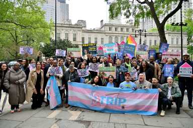 Advocates huddle in front of City Hall to rally for increased funding for trans initiatives in the city budget.