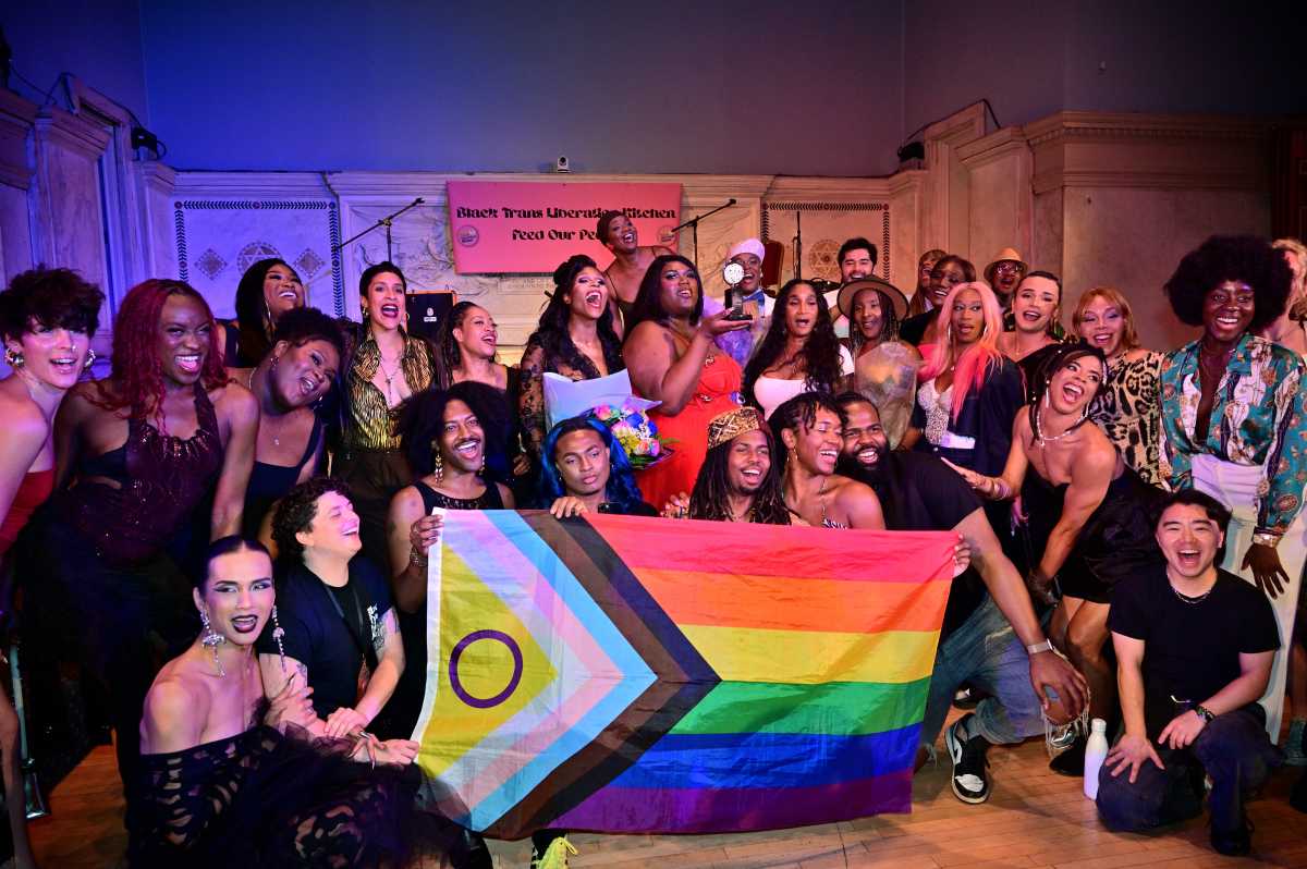Qween Jean holds her Tony award while surrounded by attendees at the "Broadway is Trans" fundraiser.