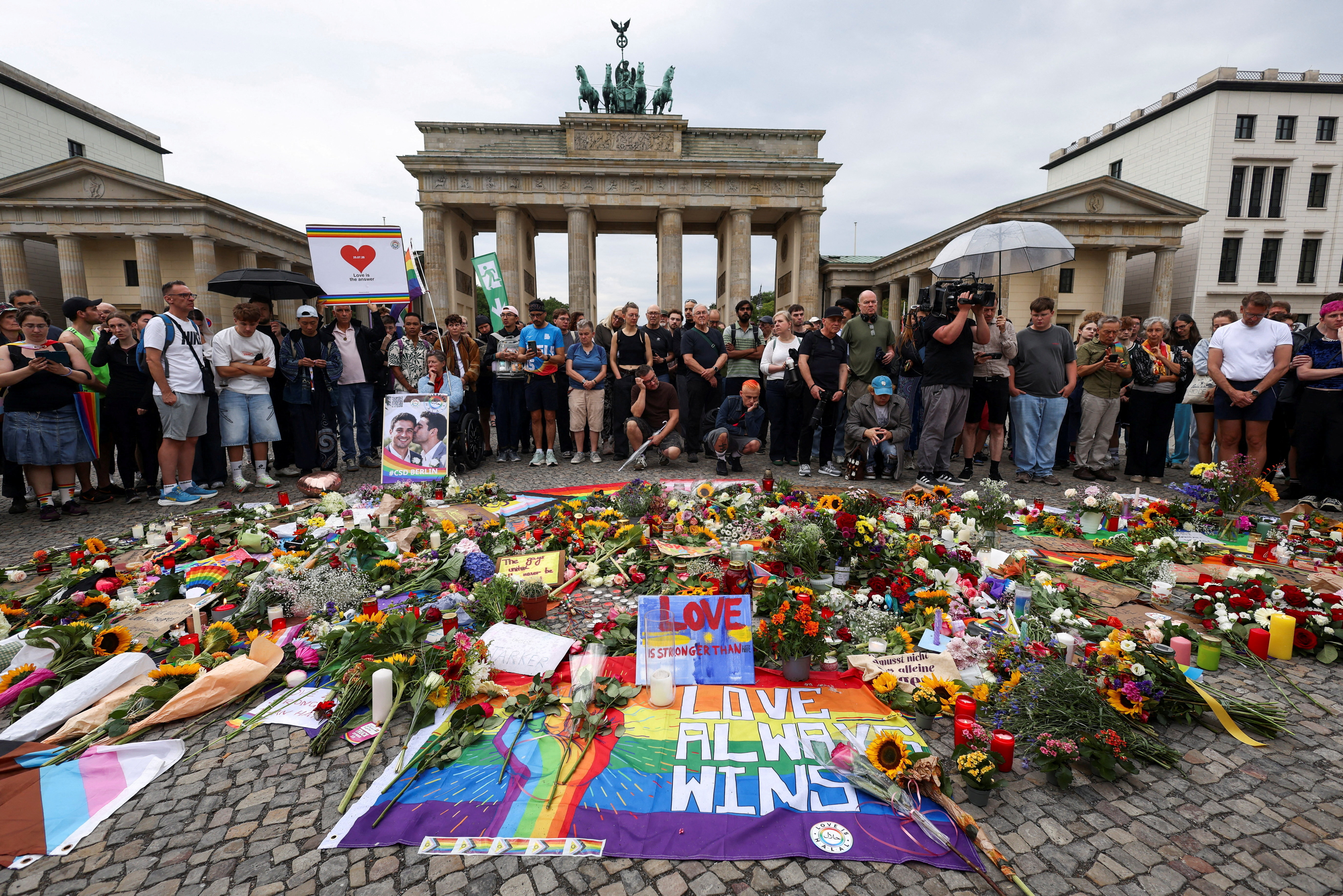 People gather around flowers, mementos, and candles in Berlin, Germany on July 26 at the Brandenburg Gate, after a deadly incident in which a vehicle crashed into a crowd near Berlin's annual Christopher Street Day Pride parade on the evening of July 25.